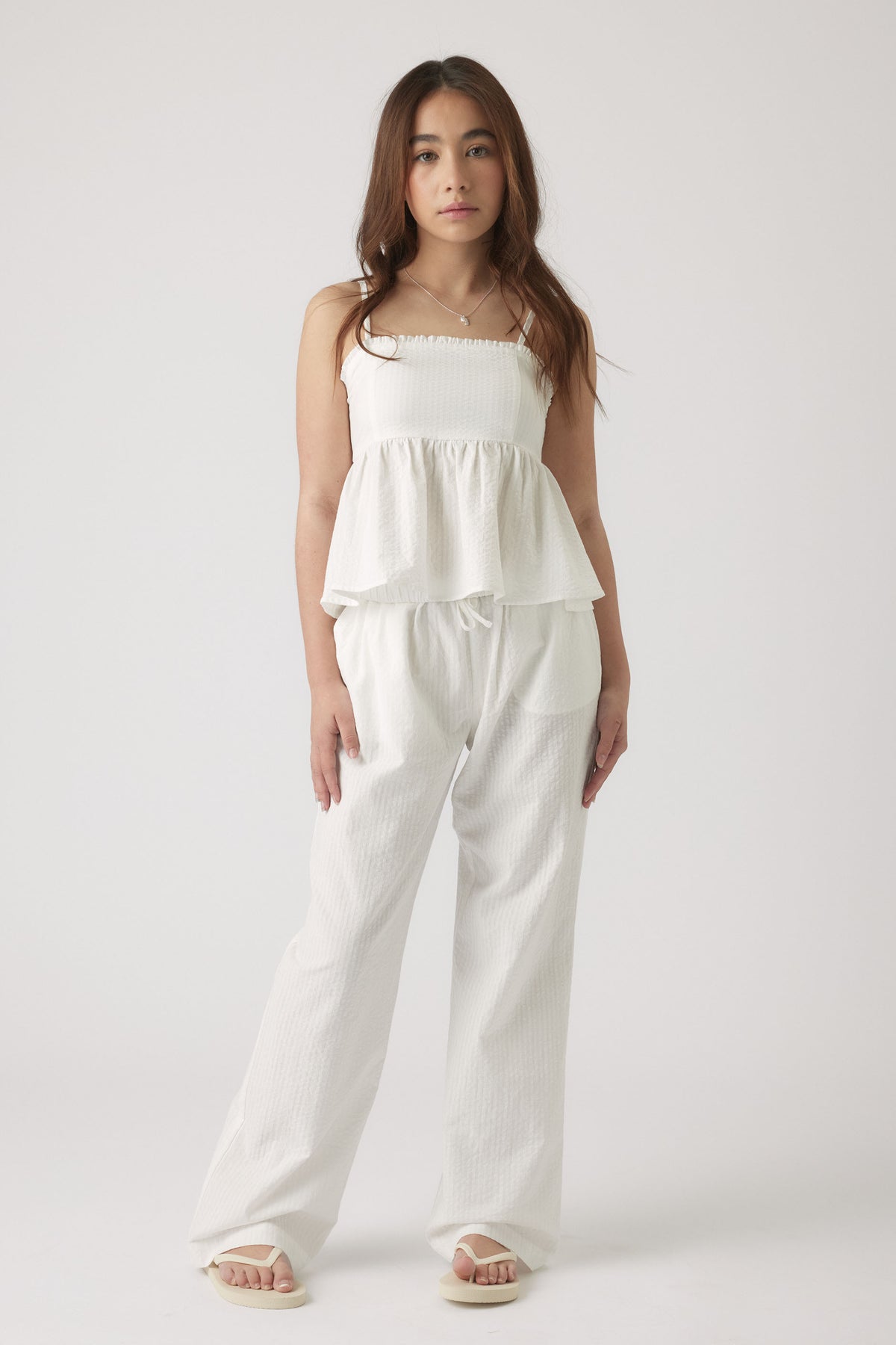 Girl wearing textured white wide-leg pants paired with a matching sleeveless top and sandals in a minimalist setting