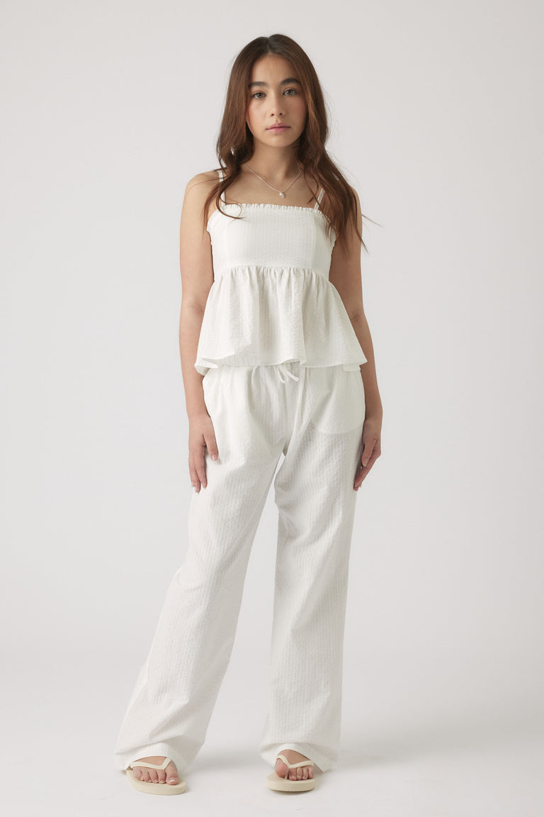 Girl wearing textured white wide-leg pants paired with a matching sleeveless top and sandals in a minimalist setting