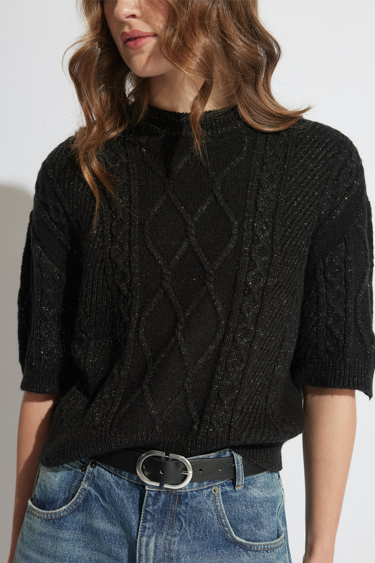 Woman wearing a textured black knit top with elbow-length sleeves, styled with a leather belt and casual blue jeans