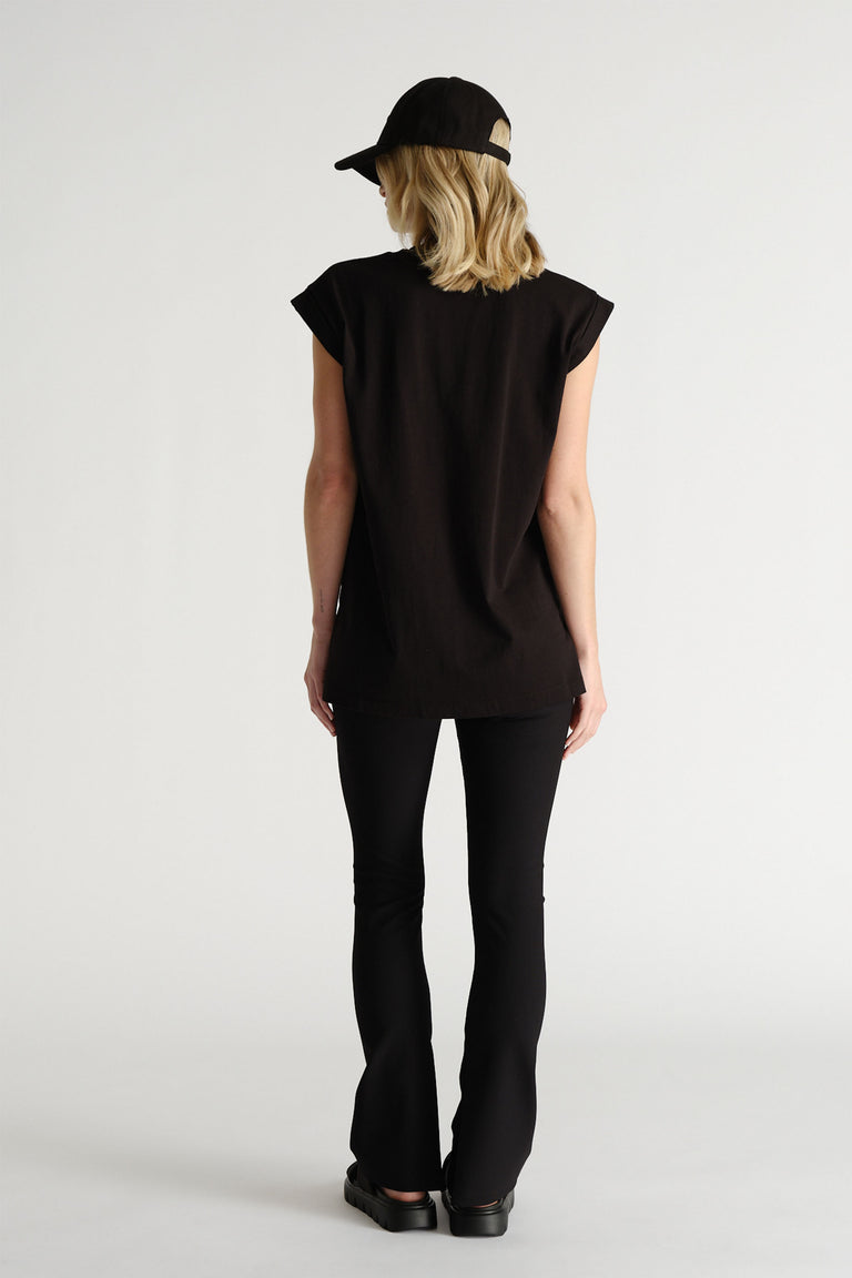 Back view of woman wearing a black sleeveless tank with structured shoulders paired with fitted black flared pants and a cap