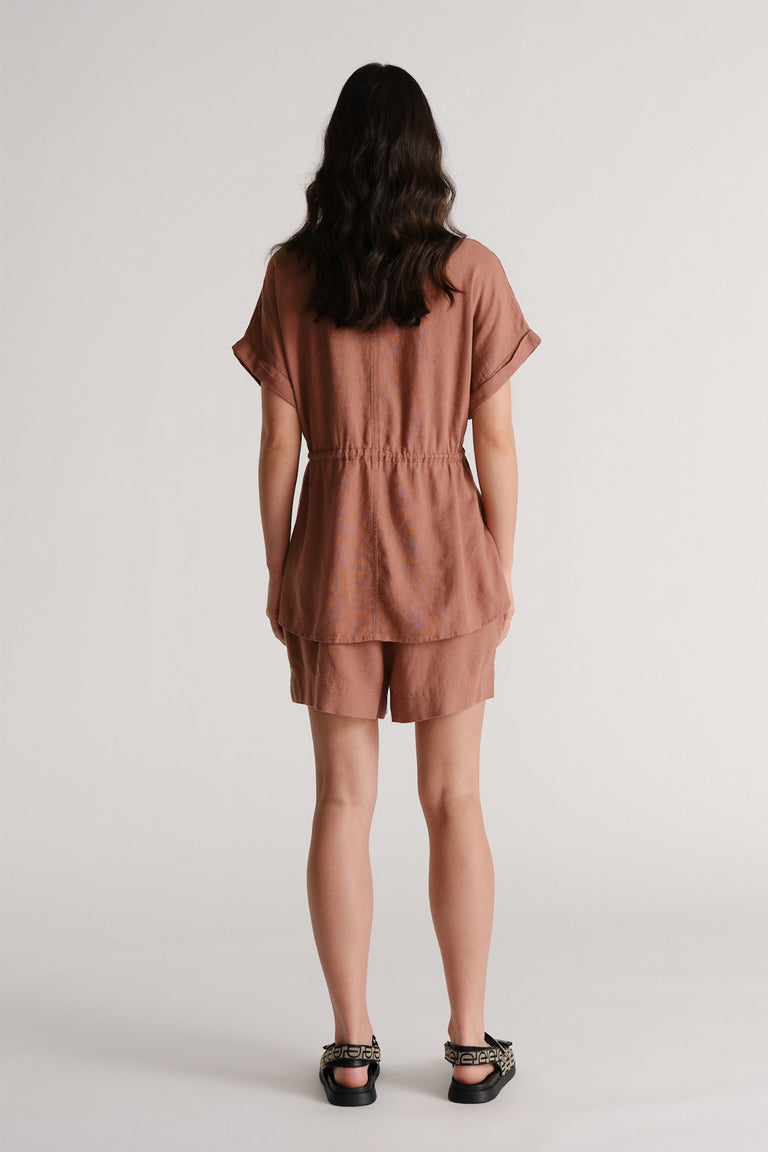 Woman wearing relaxed rosewood linen blend shorts with a matching loose top and patterned flat sandals viewed from behind