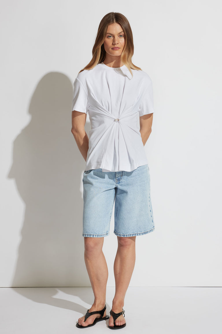 Woman wearing a white tee with metal detail at front paired with light wash denim shorts and black sandals