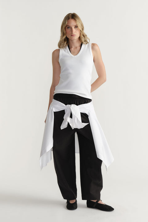 Woman wearing a white ribbed scoop tank layered over a black top, styled with black wide-leg pants and a tied white shirt waist.