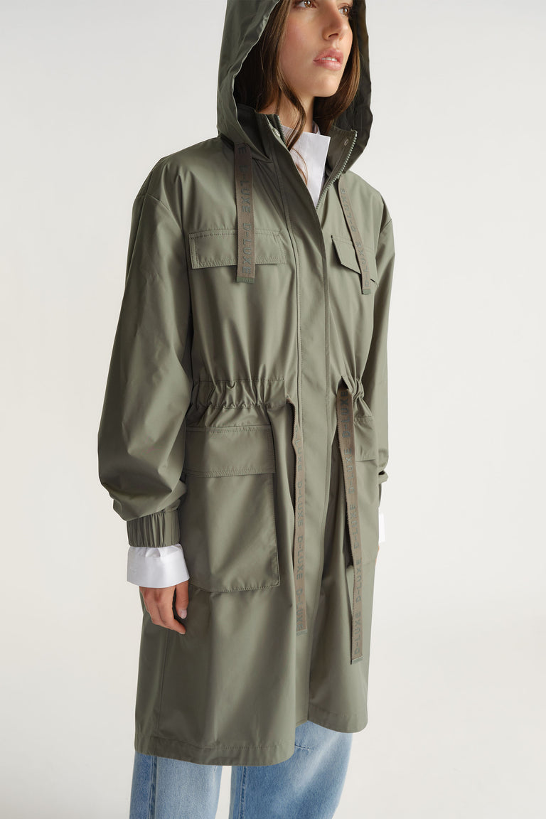 Woman wearing olive D-Luxe Rain Jacket with hood and adjustable waist paired with light denim jeans by Decjuba Australian brand