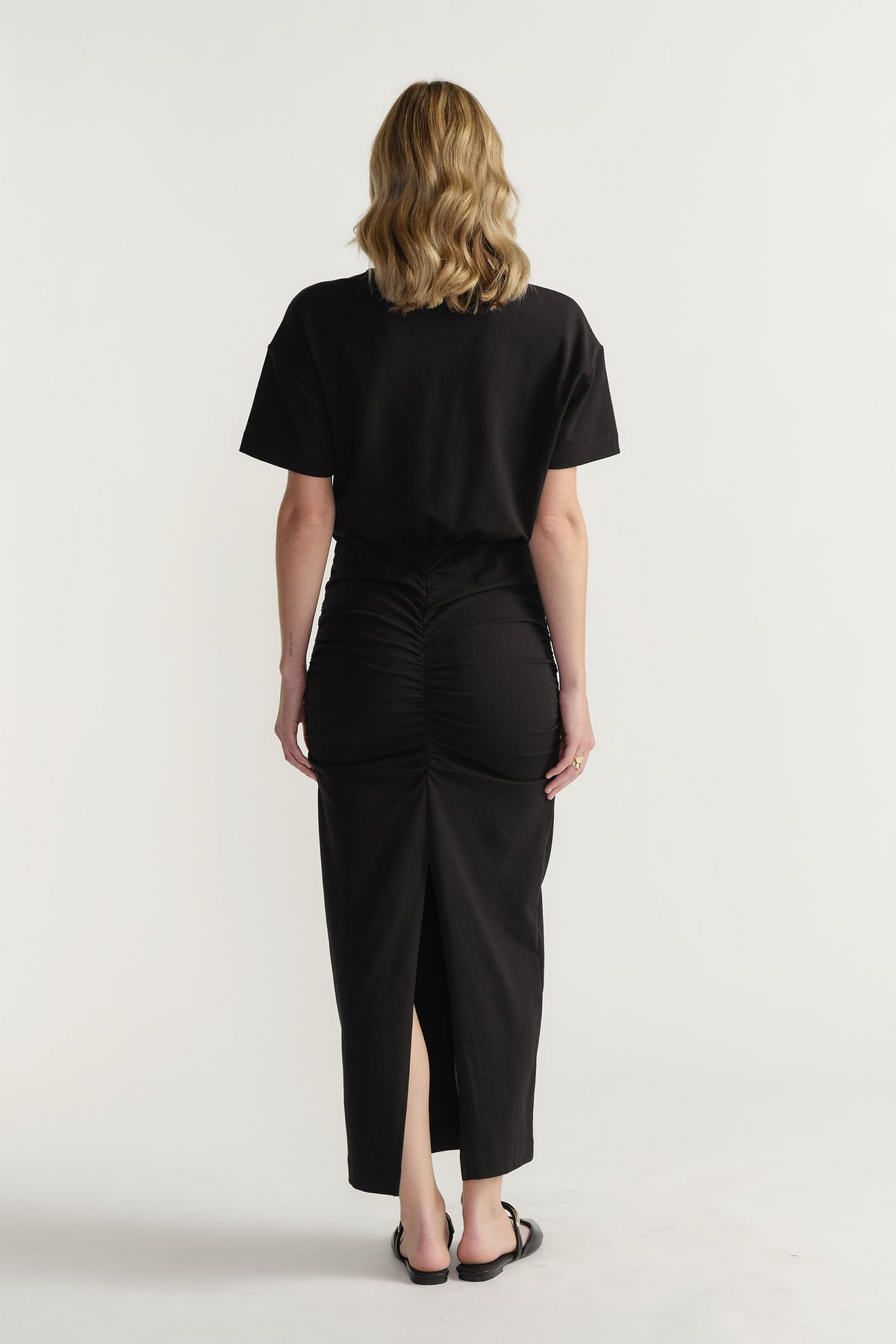 Back view of woman wearing a black ruched midi skirt paired with a relaxed short sleeve top and sandals