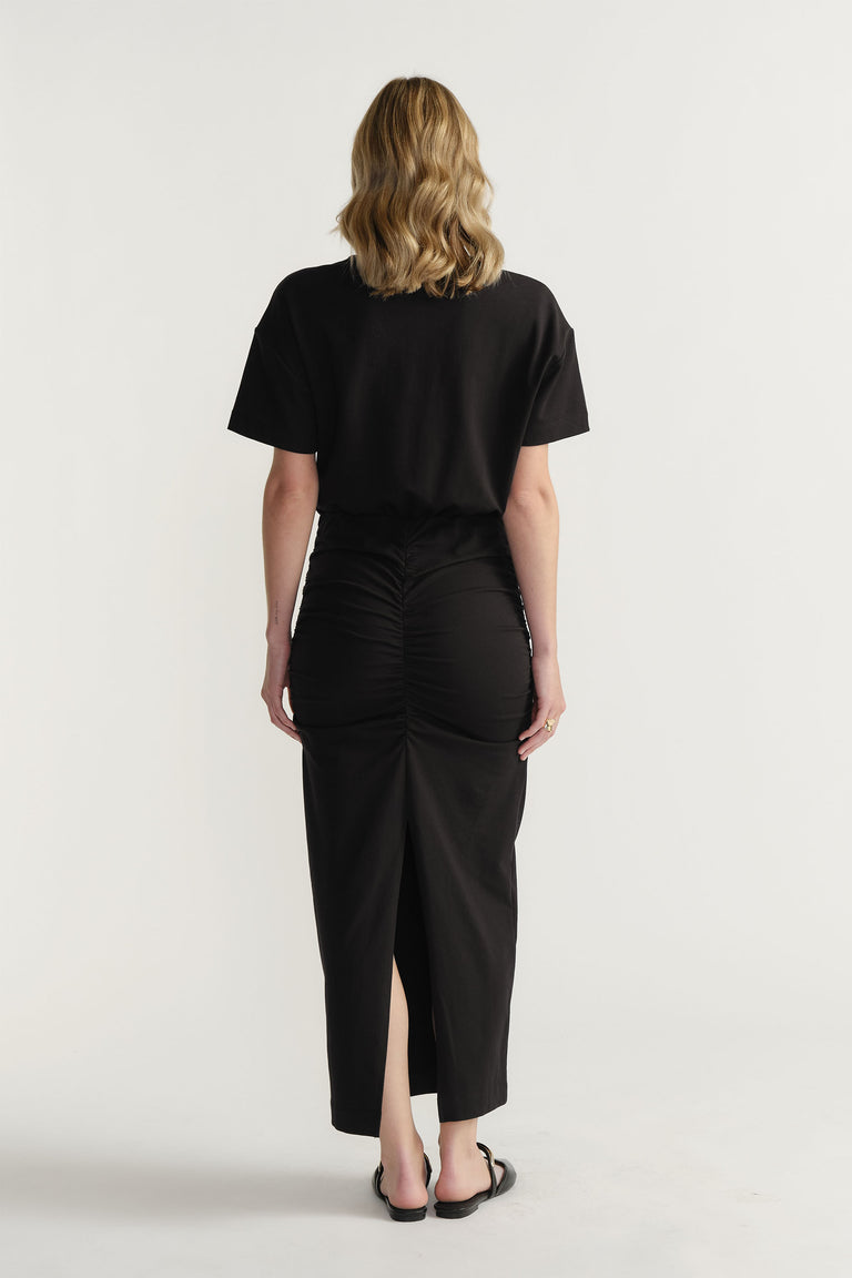Back view of woman wearing a black ruched midi skirt paired with a relaxed short sleeve top and sandals