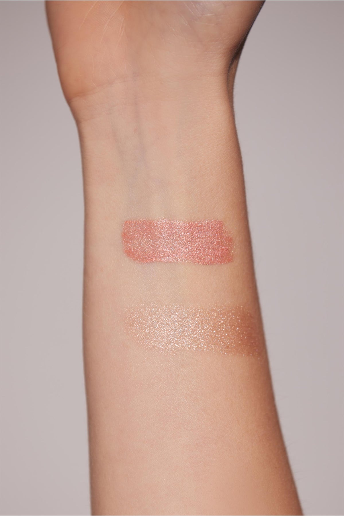 Two shimmering highlighter swatches on a model's wrist in rosy and champagne shades