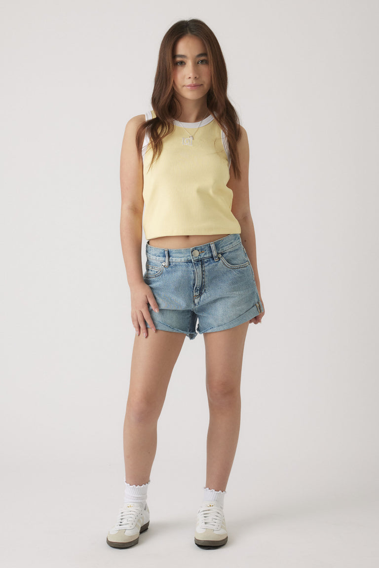 Teen girl wearing a pale yellow sleeveless tank top paired with light blue denim shorts and white sneakers.