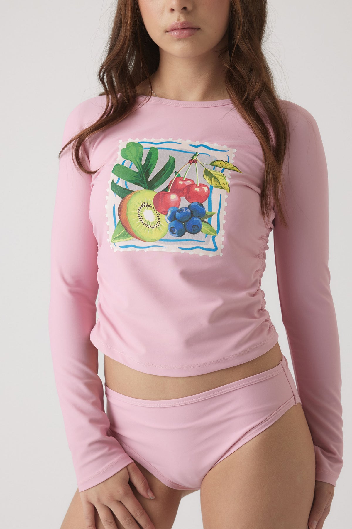Girl wearing a pink long sleeve swim top with fruit print and matching swim bottoms for a fun, vibrant look
