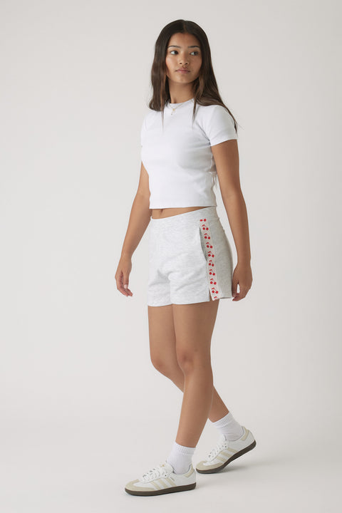 Teen girl wearing light grey sweat shorts with cherry print side stripes and a fitted white crop top with casual sneakers