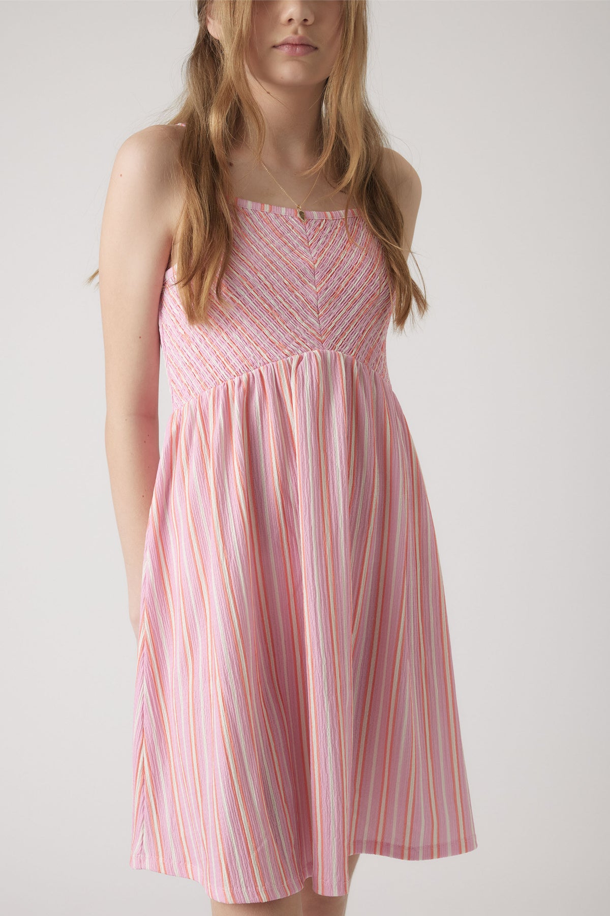 Girl wearing a pink shirred dress with thin straps and vertical multicolor stripes for a fresh summer look