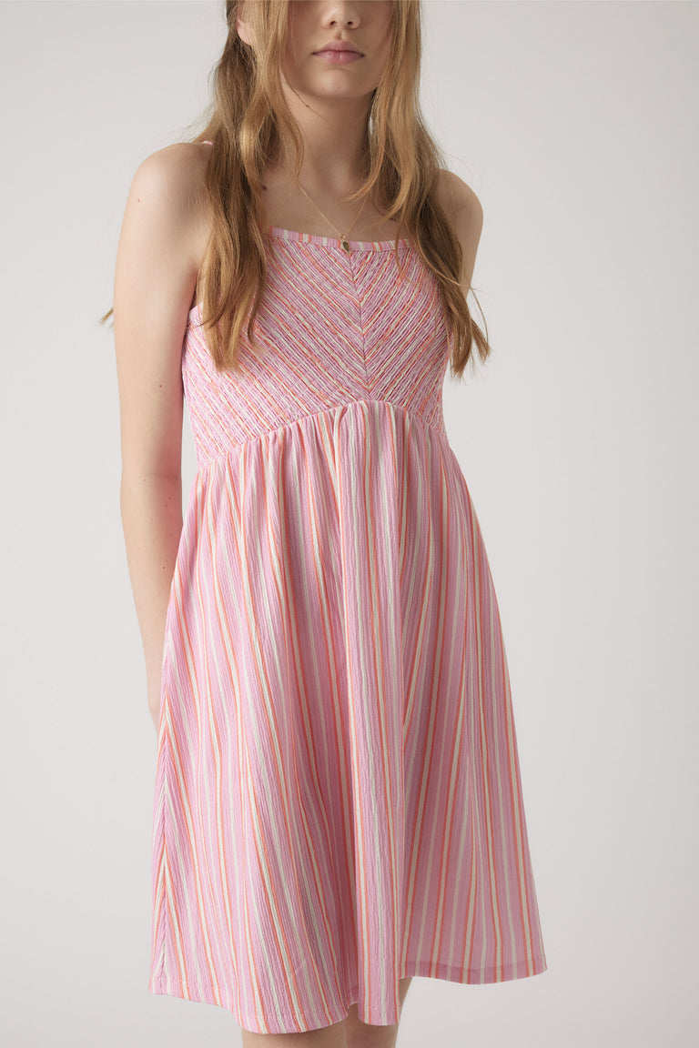 Girl wearing a pink shirred dress with thin straps and vertical multicolor stripes for a fresh summer look