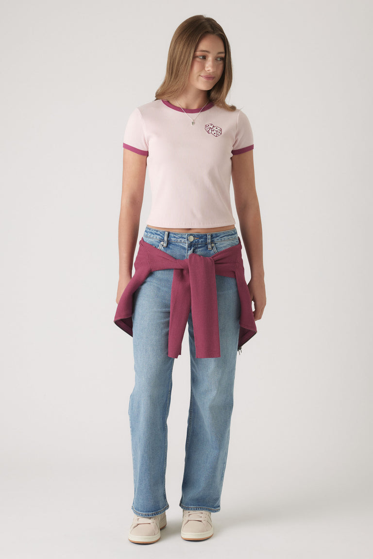 Teen girl wearing a pink cropped ringer tee with heart detail, light blue jeans, and a maroon sweater tied at the waist