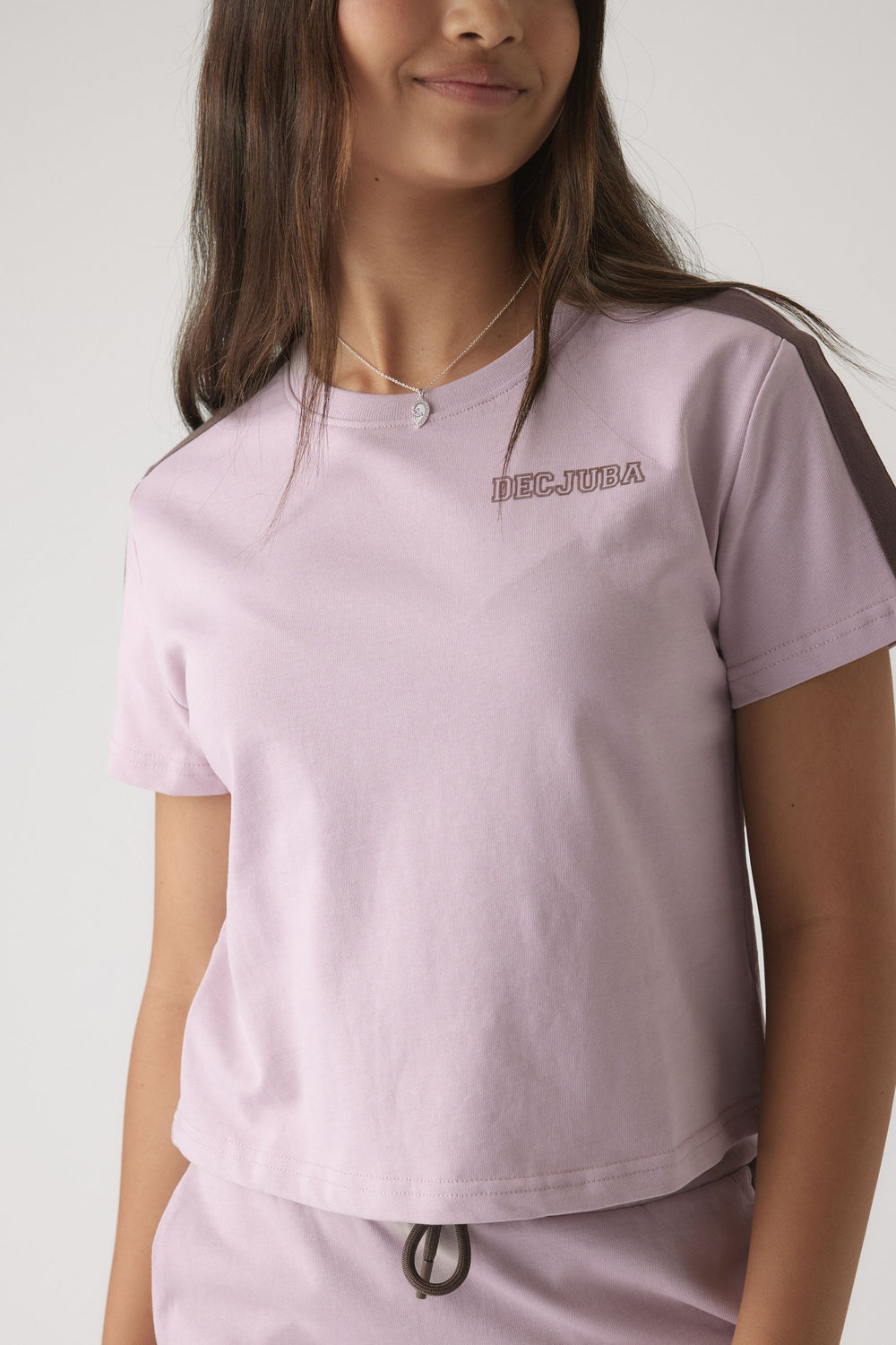Close-up of girl wearing a relaxed lilac boxy tee with contrast racing stripes on sleeves and casual drawstring pants