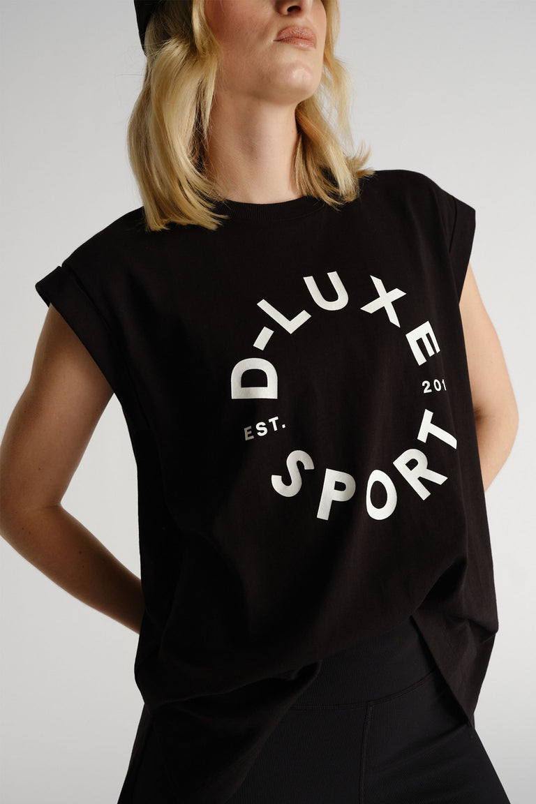 Woman wearing a black sleeveless tank with bold white circular text paired with fitted black pants for a sporty look