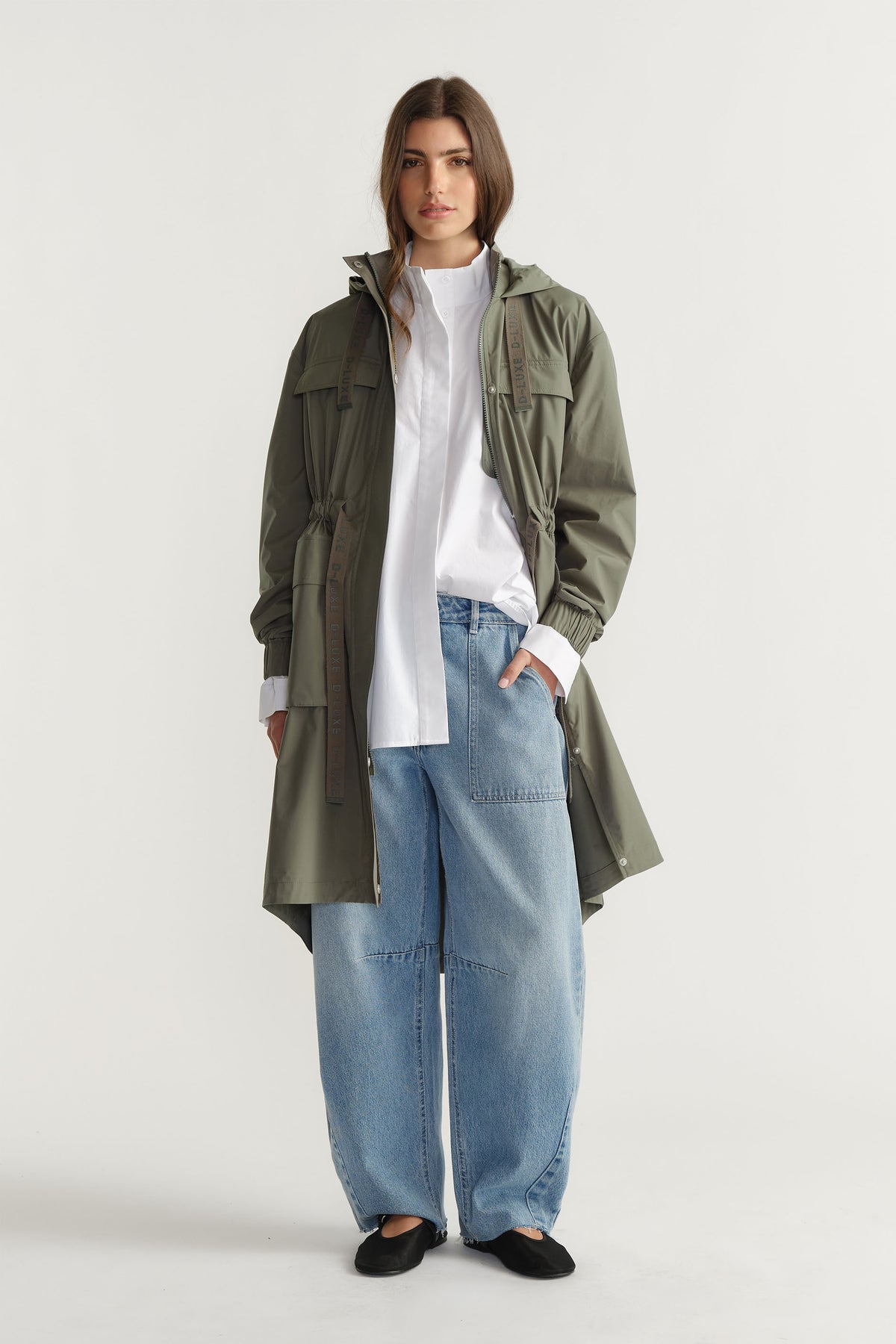 Woman wearing D-Luxe Rain Jacket in muted olive with gathered waist and hood styled with a white shirt and wide-leg jeans by Decjuba