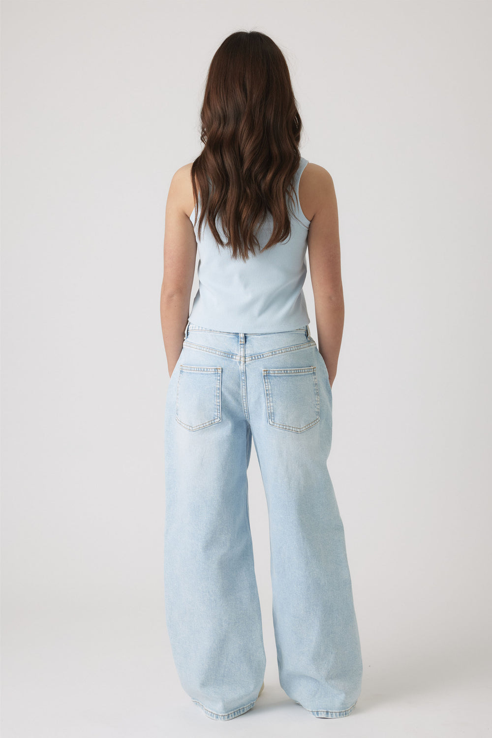 Rear view of girl wearing a pale blue sleeveless top paired with relaxed light wash wide-leg jeans