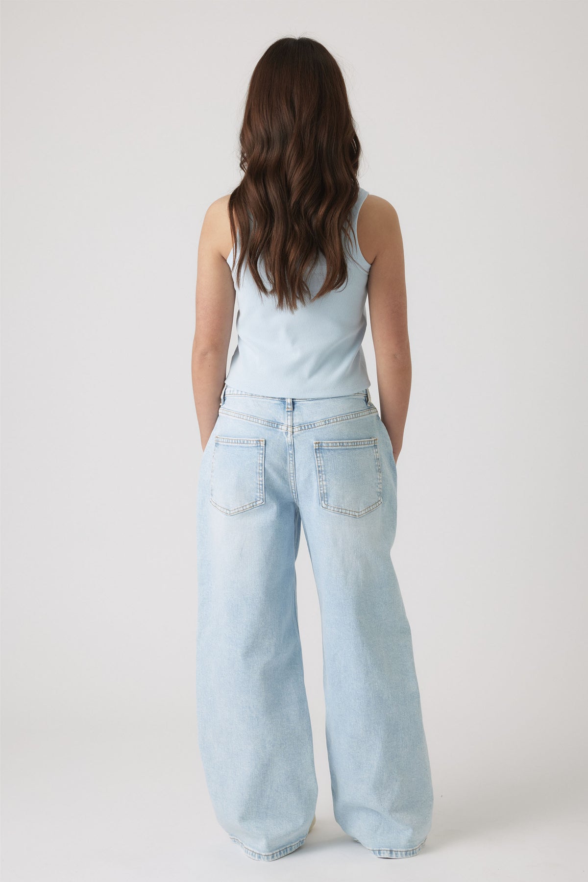 Rear view of girl wearing a pale blue sleeveless top paired with relaxed light wash wide-leg jeans