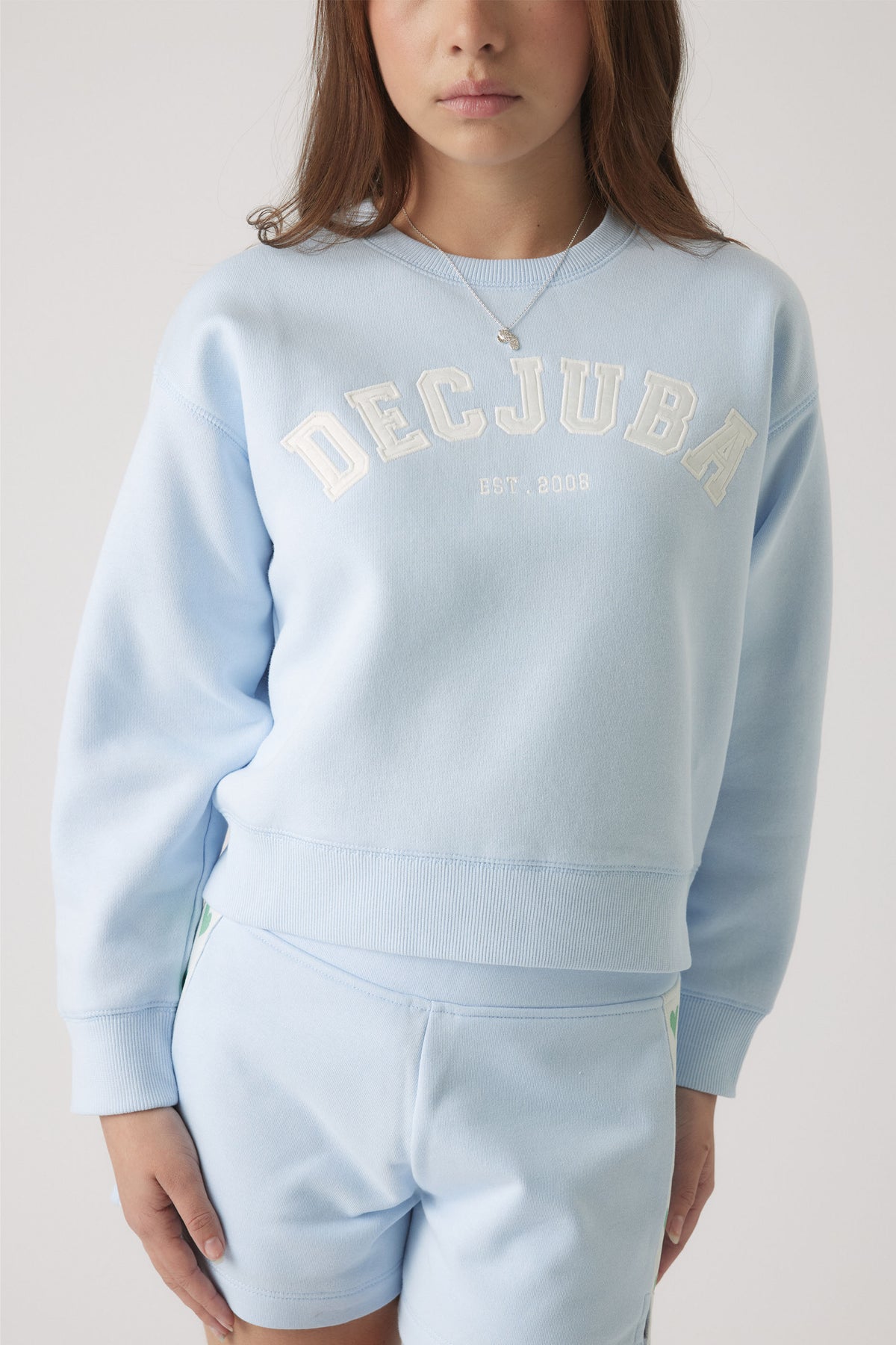 Girl wearing a pale blue sweatshirt with white logo lettering paired with matching shorts for a relaxed, casual look.