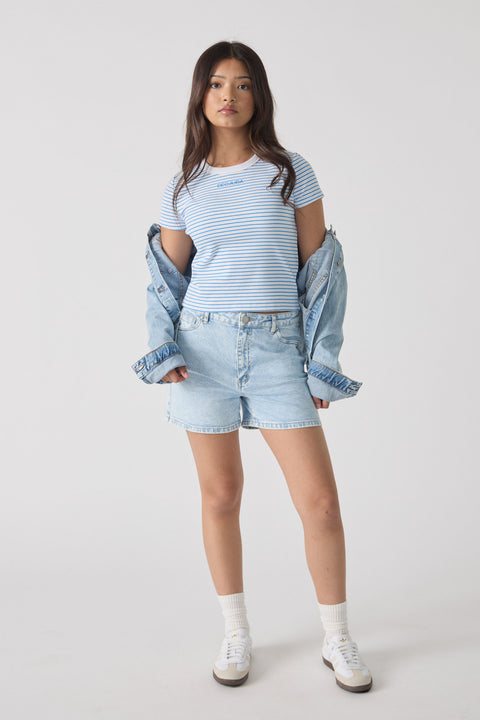 Teen girl wearing light blue denim shorts with a striped tee and denim jacket draped over her arms, casual style.