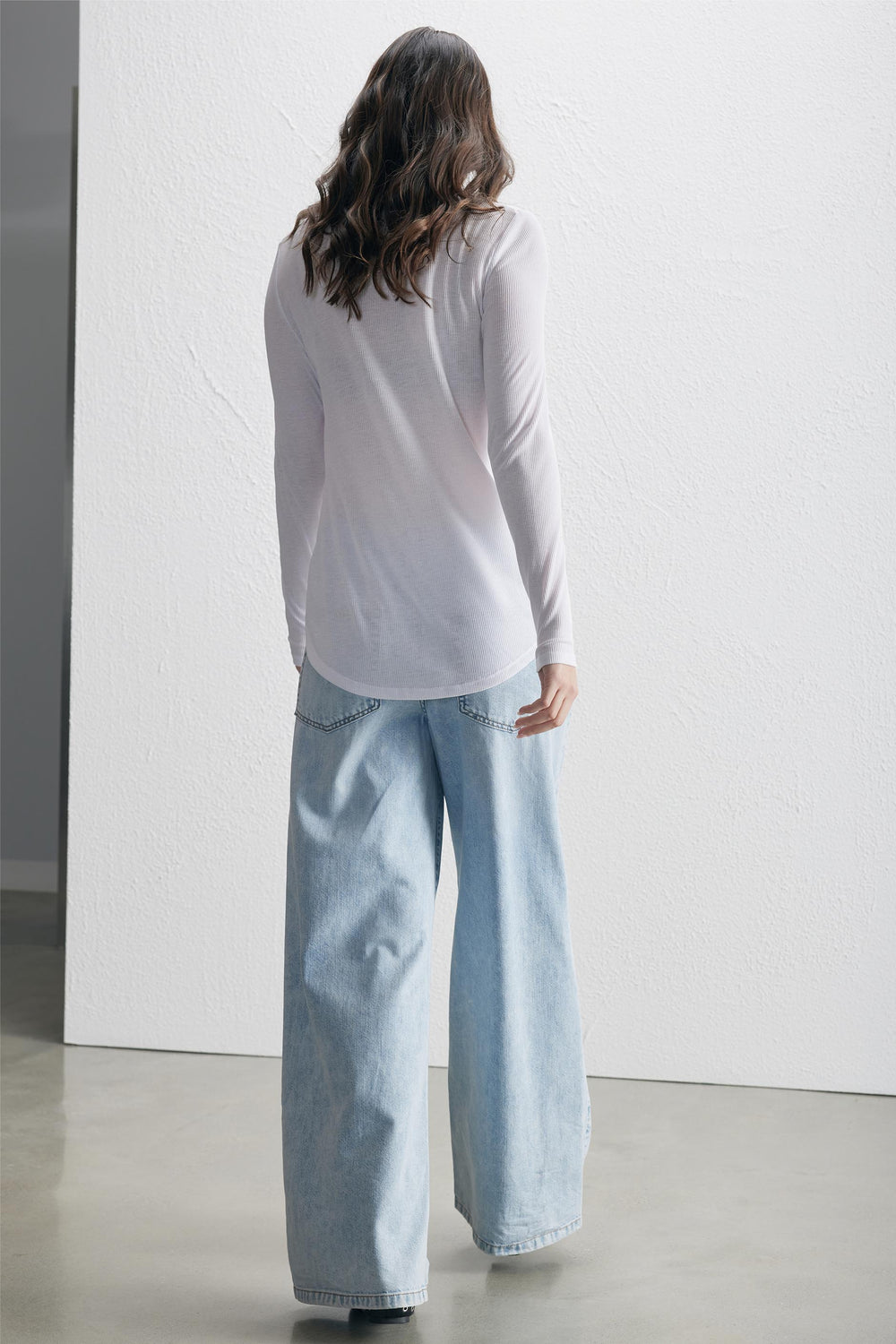 Woman wearing a bright white long sleeve tee paired with light blue wide-leg denim jeans, standing indoors