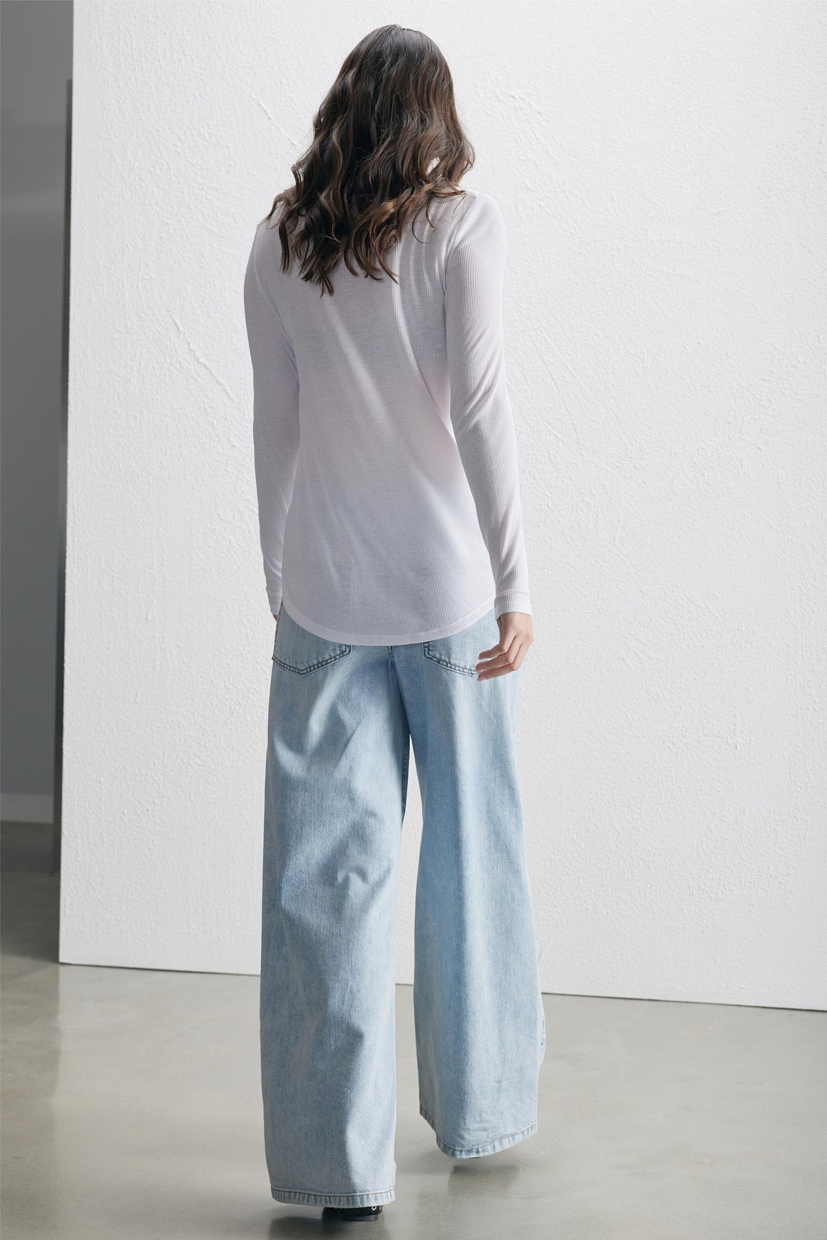 Woman wearing a bright white long sleeve tee paired with light blue wide-leg denim jeans, standing indoors