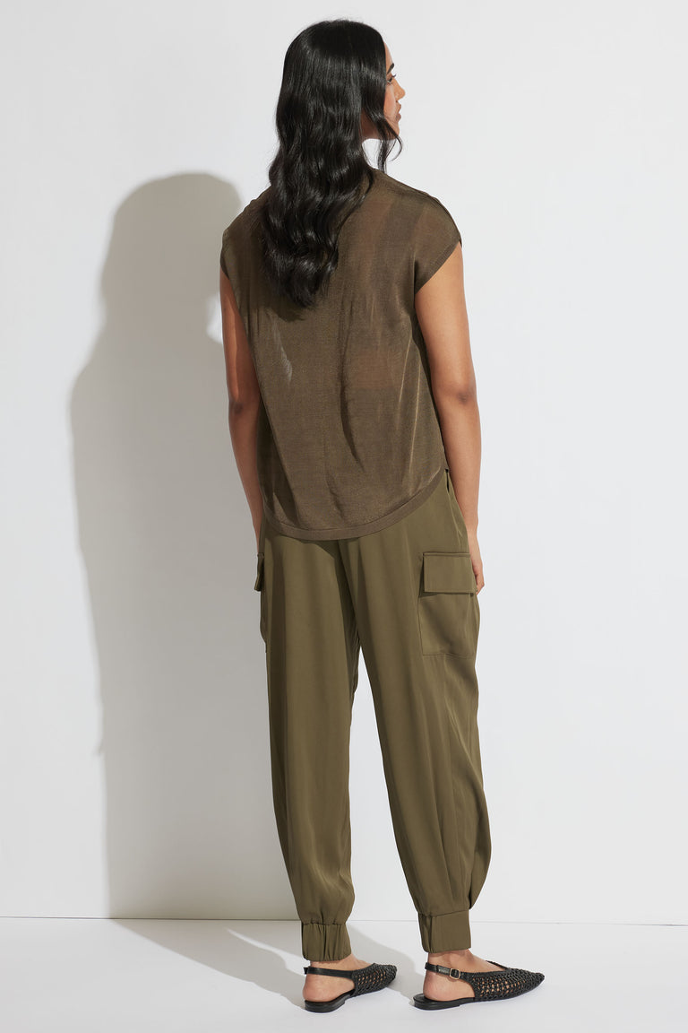 Rear view portrait of model wearing olive Tatum Knit Tee with relaxed fit and sheer fabric, styled with cargo pants and flats