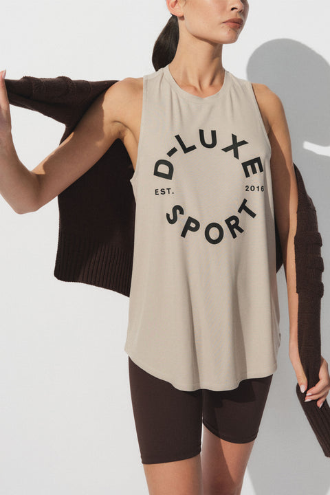 Woman wearing a beige sleeveless tank with bold black lettering paired with dark fitted bike shorts and a sweater draped on shoulders