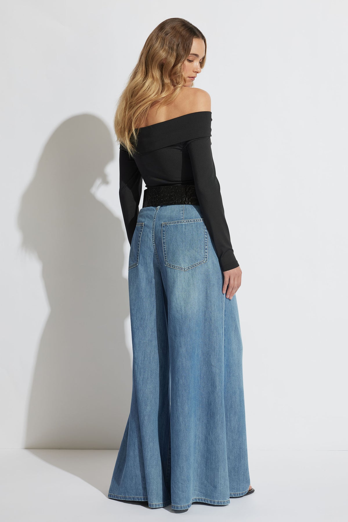 Woman wearing an off-shoulder black top paired with wide-leg light blue denim jeans, shown from the back.