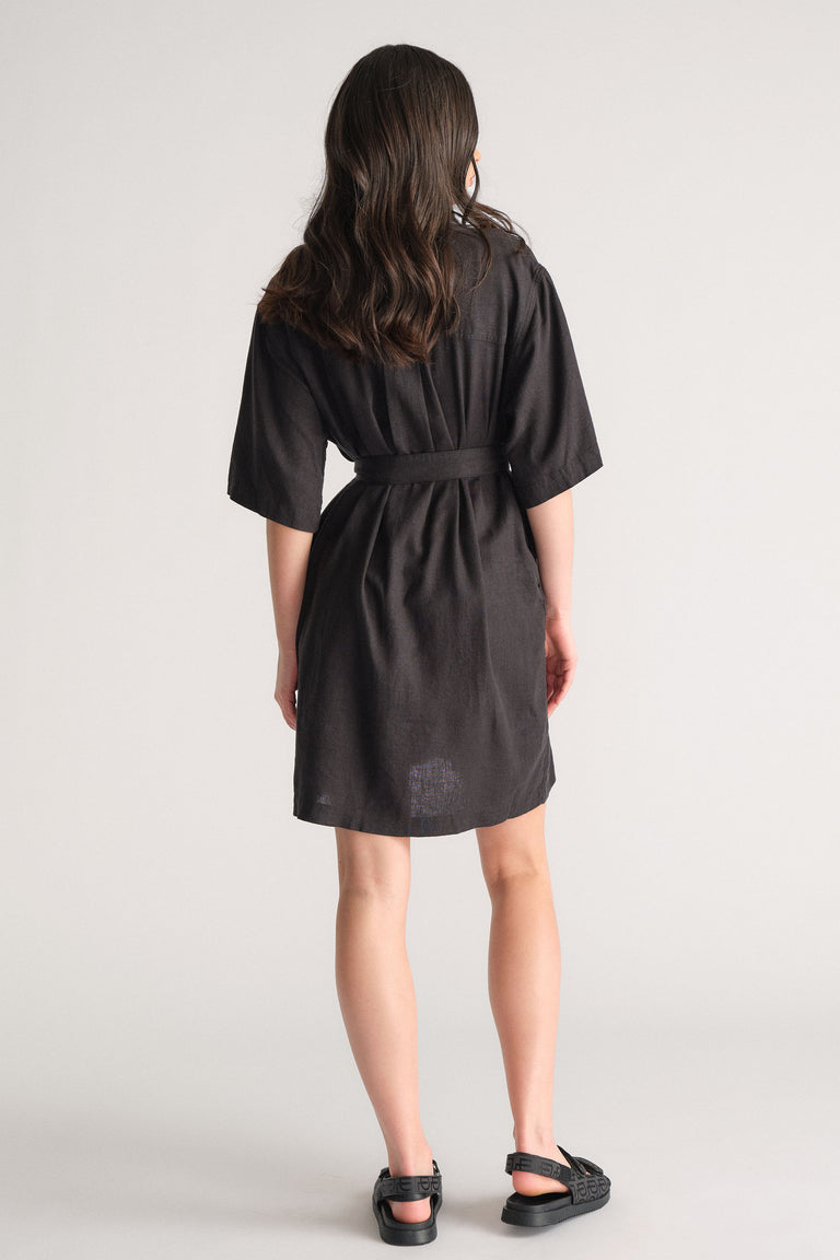 Woman wearing a black linen blend short dress with a relaxed fit belt and half-length sleeves paired with black sandals