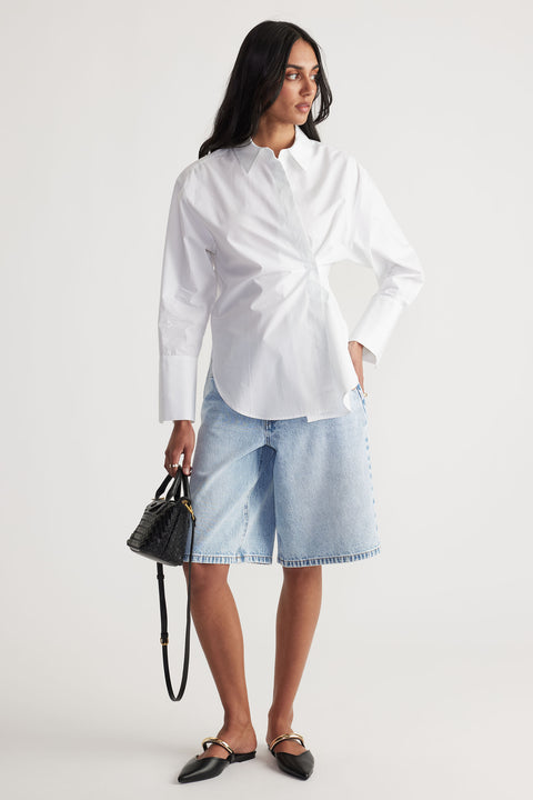 Model wears a white Ivy Button Shirt in portrait, gallery position 1, paired with casual denim shorts and black handbag.