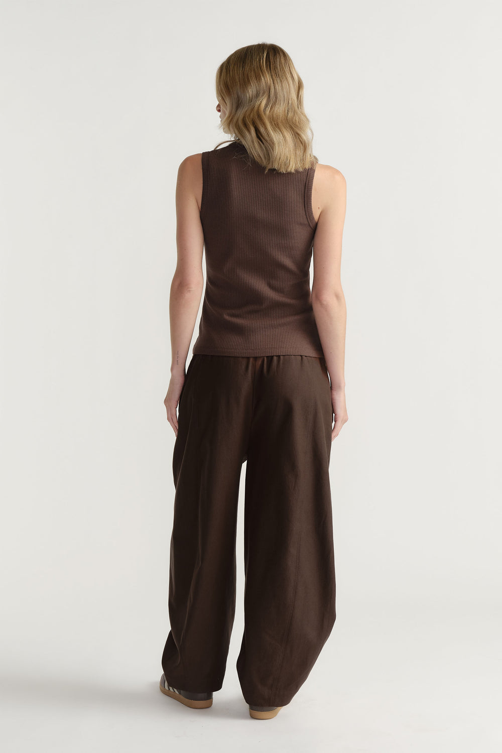 Woman wearing a dark brown ribbed tank top paired with loose, wide-leg trousers for a relaxed, stylish outfit.