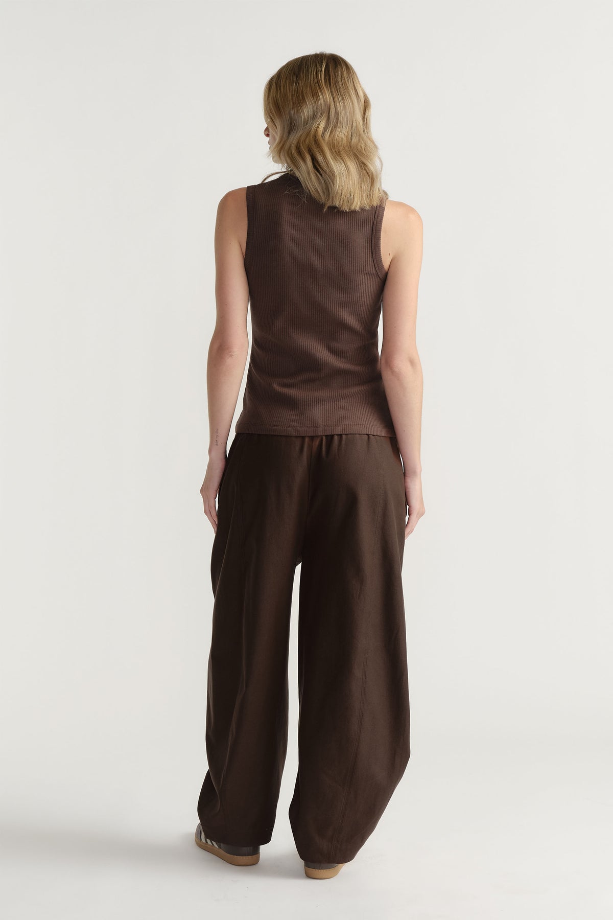 Woman wearing a dark brown ribbed tank top paired with loose, wide-leg trousers for a relaxed, stylish outfit.