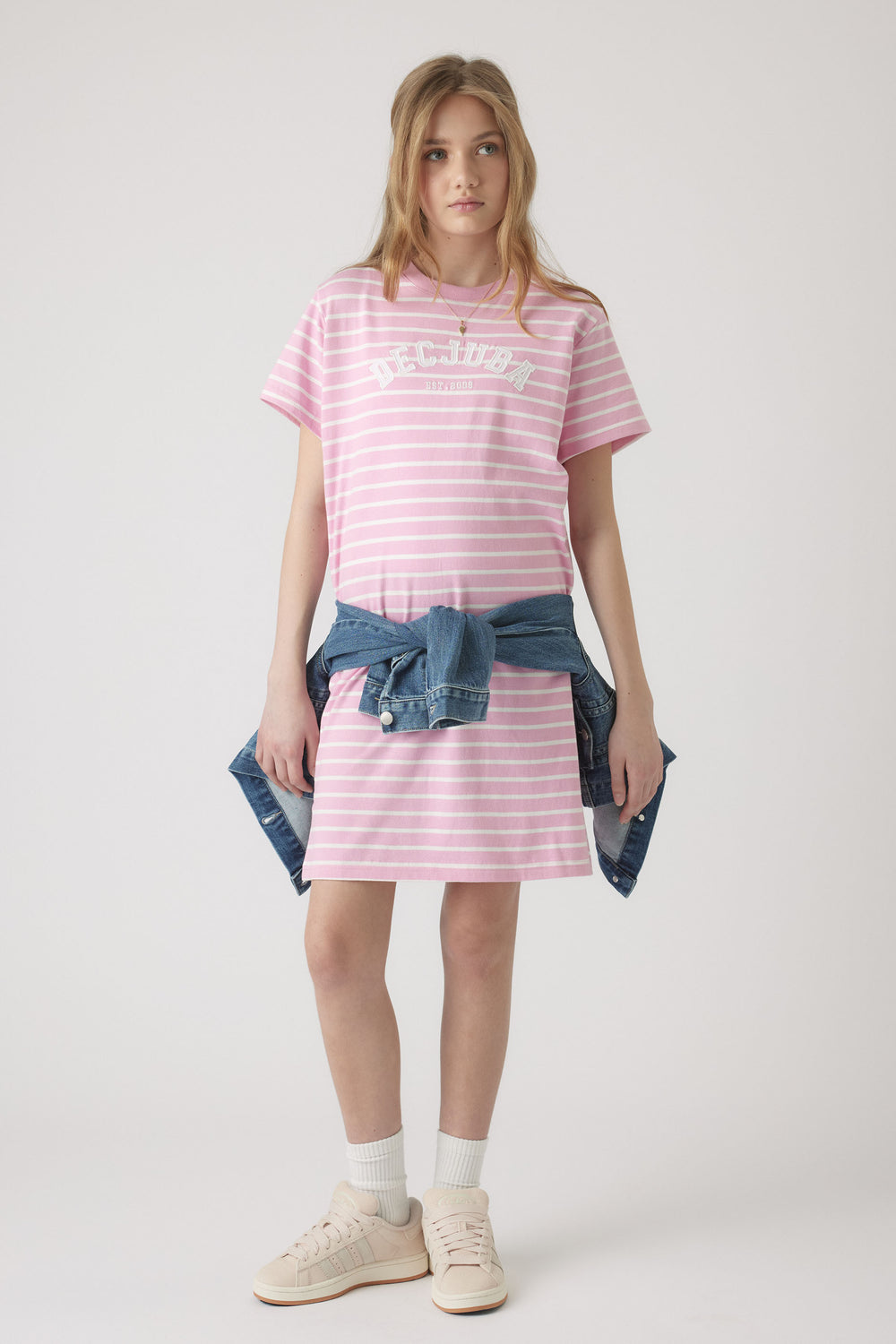 Girl wearing a relaxed pink and white striped rugby tee dress with a tied denim jacket and casual sneakers