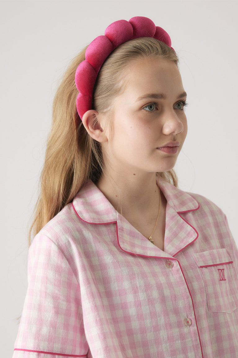 Girl wearing a bright pink padded headband paired with a soft pink gingham shirt with contrast trim detail.