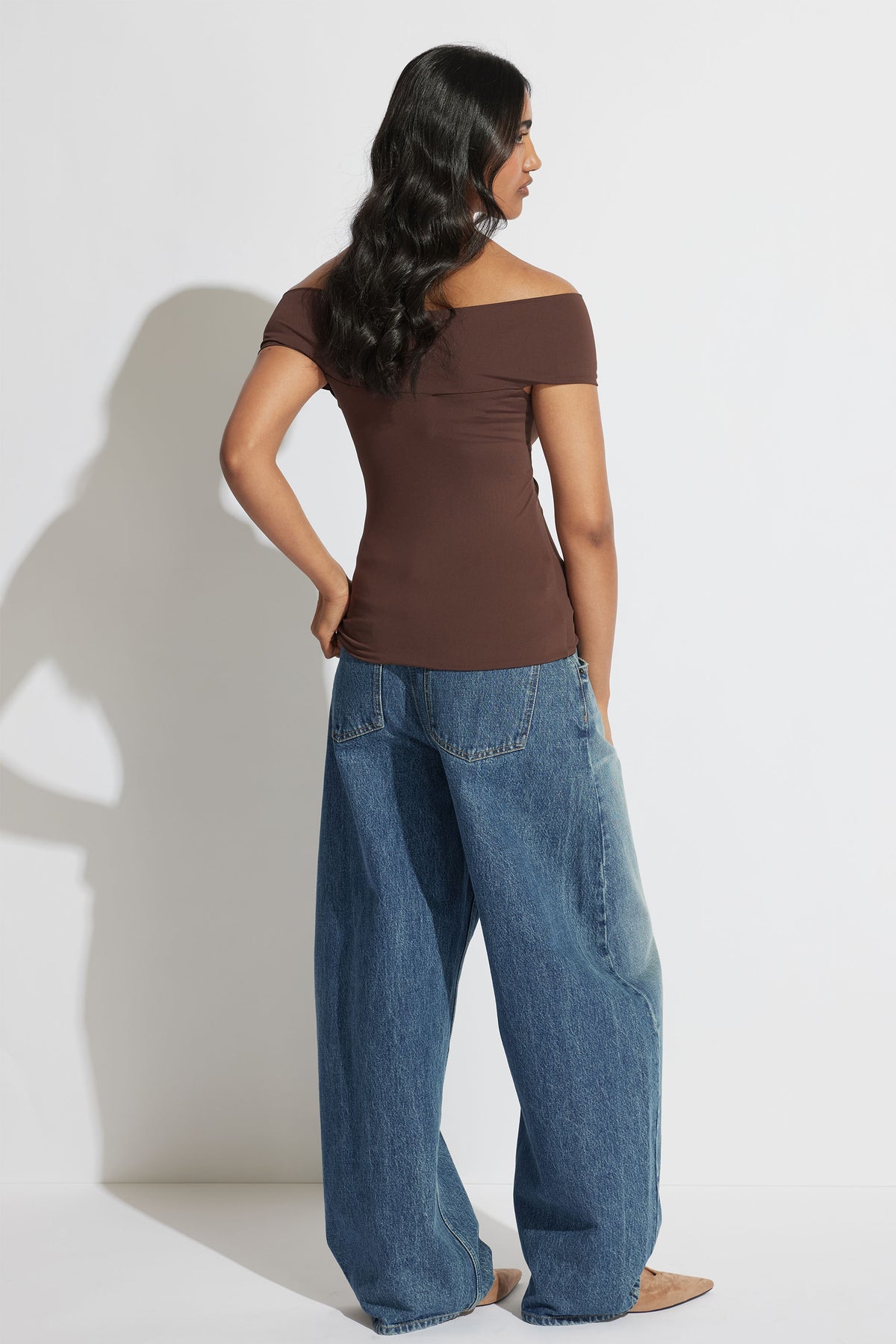 Woman wearing Amy Off Shoulder Twist Top in brown with denim wide-leg jeans, shown in portrait orientation gallery image 3.