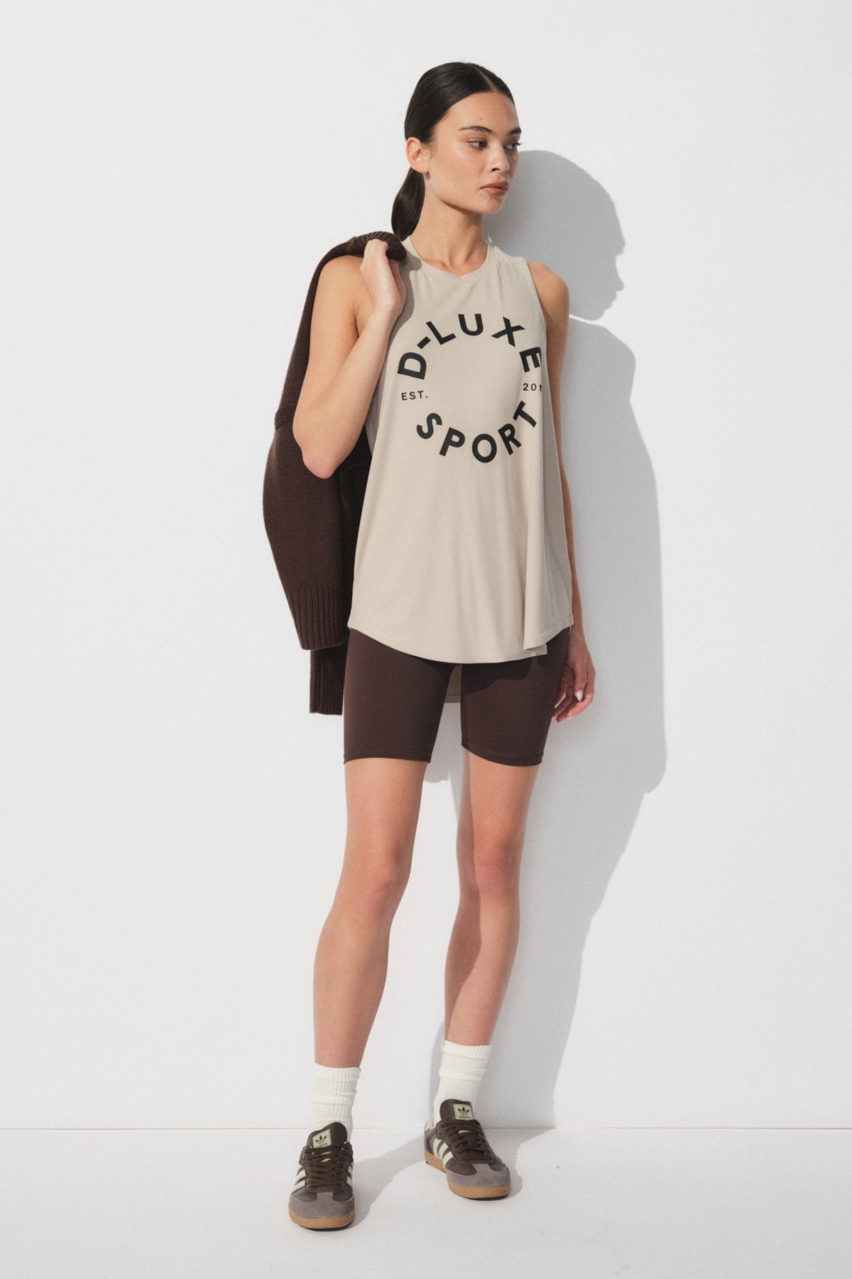 Woman wearing a relaxed beige sleeveless tank with bold text paired with dark fitted bike shorts for a sporty casual look
