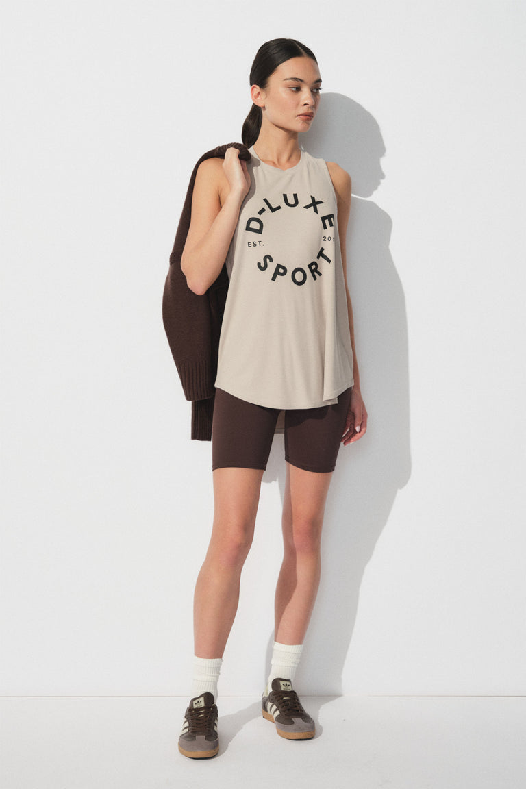 Woman wearing a relaxed beige sleeveless tank with bold text paired with dark fitted bike shorts for a sporty casual look