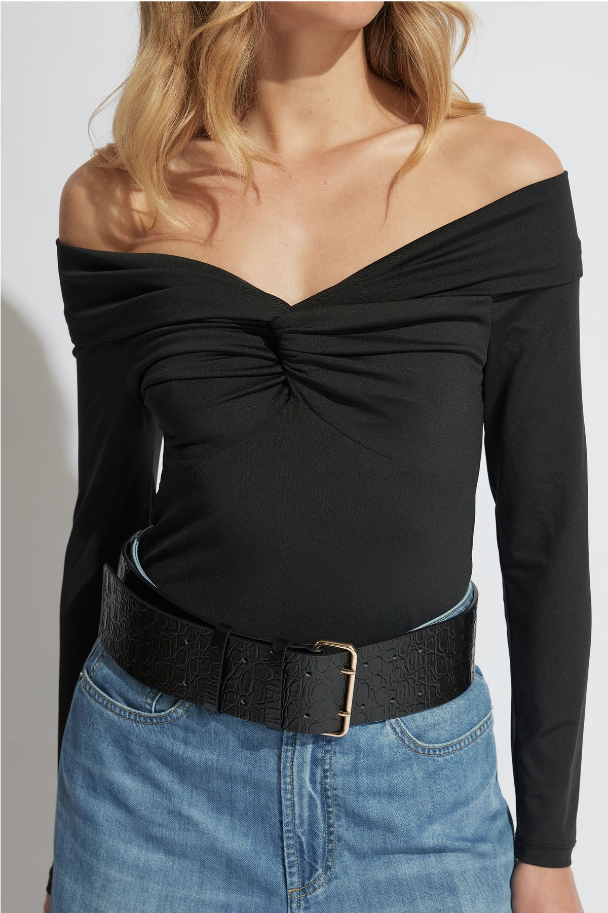 Woman wearing a black off-shoulder twisted long sleeve top paired with high-rise blue denim jeans and a wide belt