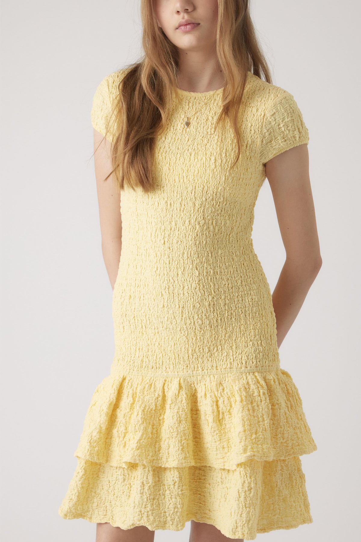 Girl wearing a textured yellow shirred dress with cap sleeves and a double-layered ruffle hem for a playful look