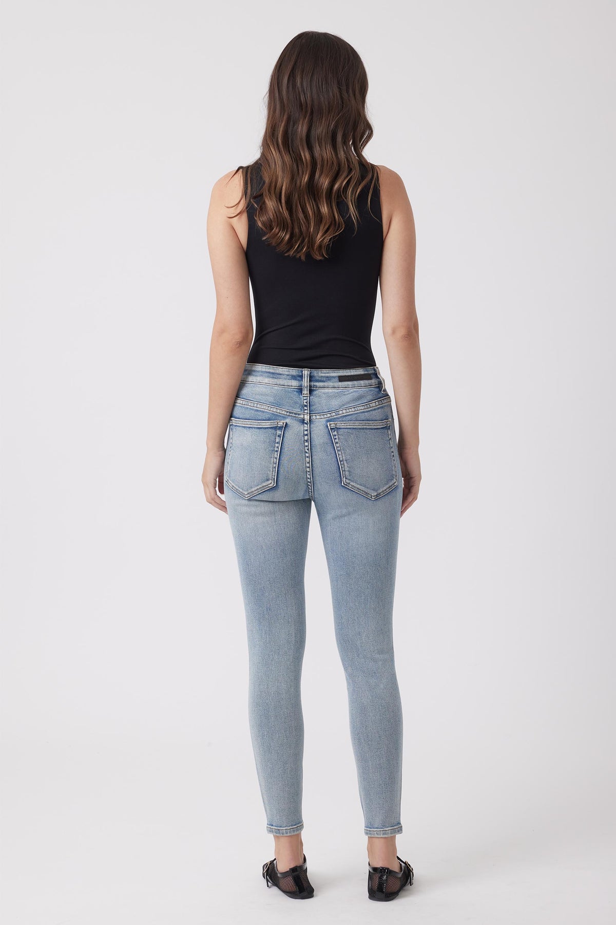 Light wash high-rise skinny jeans styled with a black sleeveless top and casual black shoes for everyday wear.