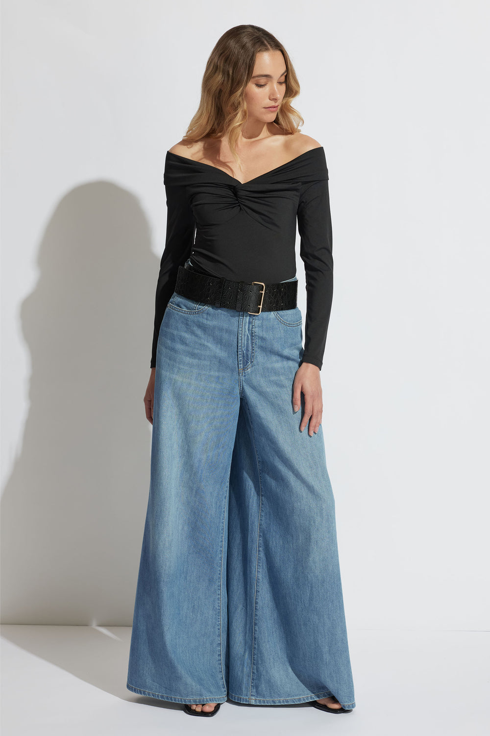 Woman wearing a black off-shoulder long sleeve top paired with wide-leg light blue denim jeans and a black belt