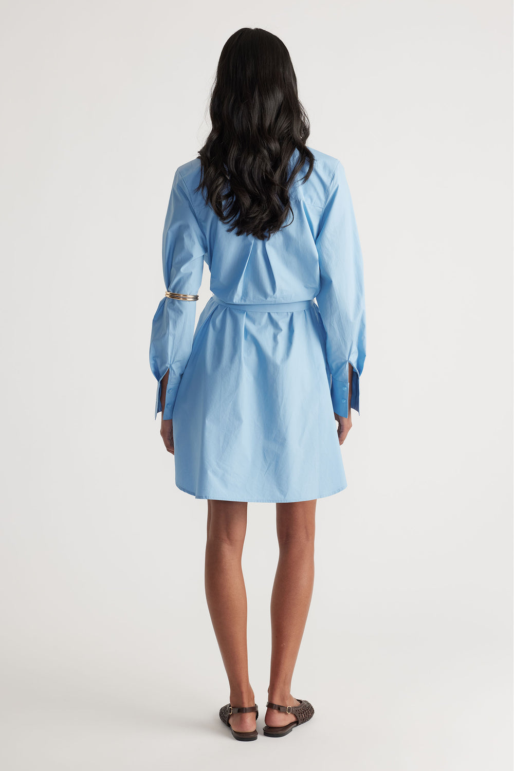 Back view of woman wearing a sky blue mini shirt dress with a tailored waist and long sleeves paired with flats