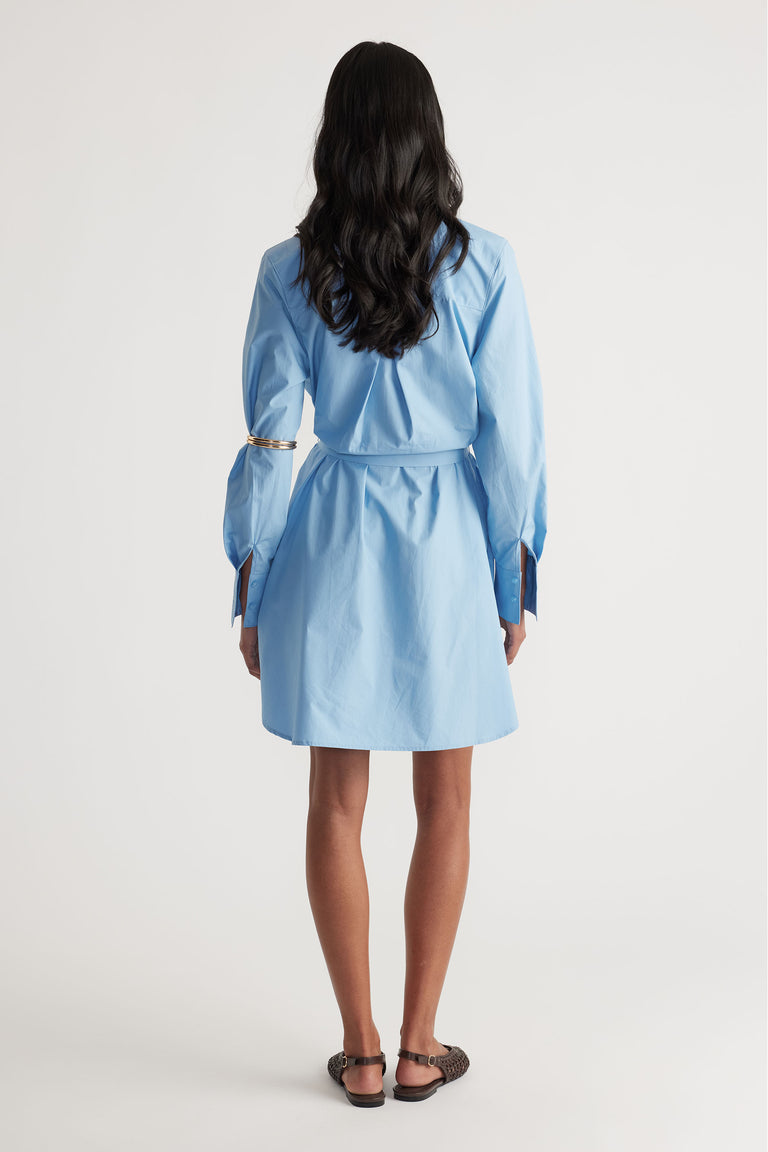 Back view of woman wearing a sky blue mini shirt dress with a tailored waist and long sleeves paired with flats