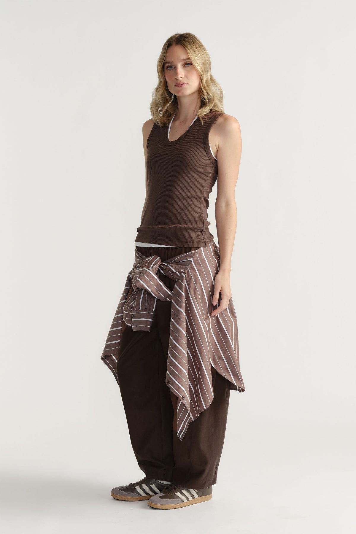 Woman wearing a ribbed brown scoop tank with relaxed dark pants and a striped shirt tied around the waist