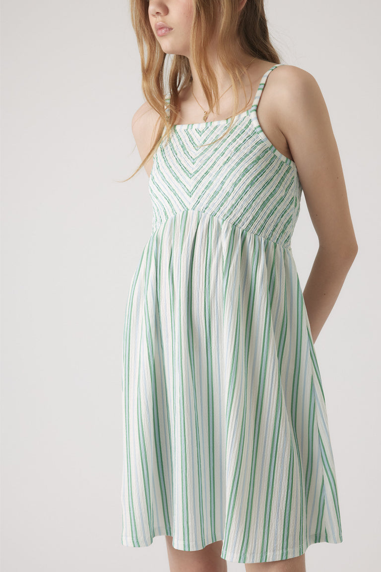 Girl wearing a lightweight green and white striped shirred dress with thin straps and a flowing skirt