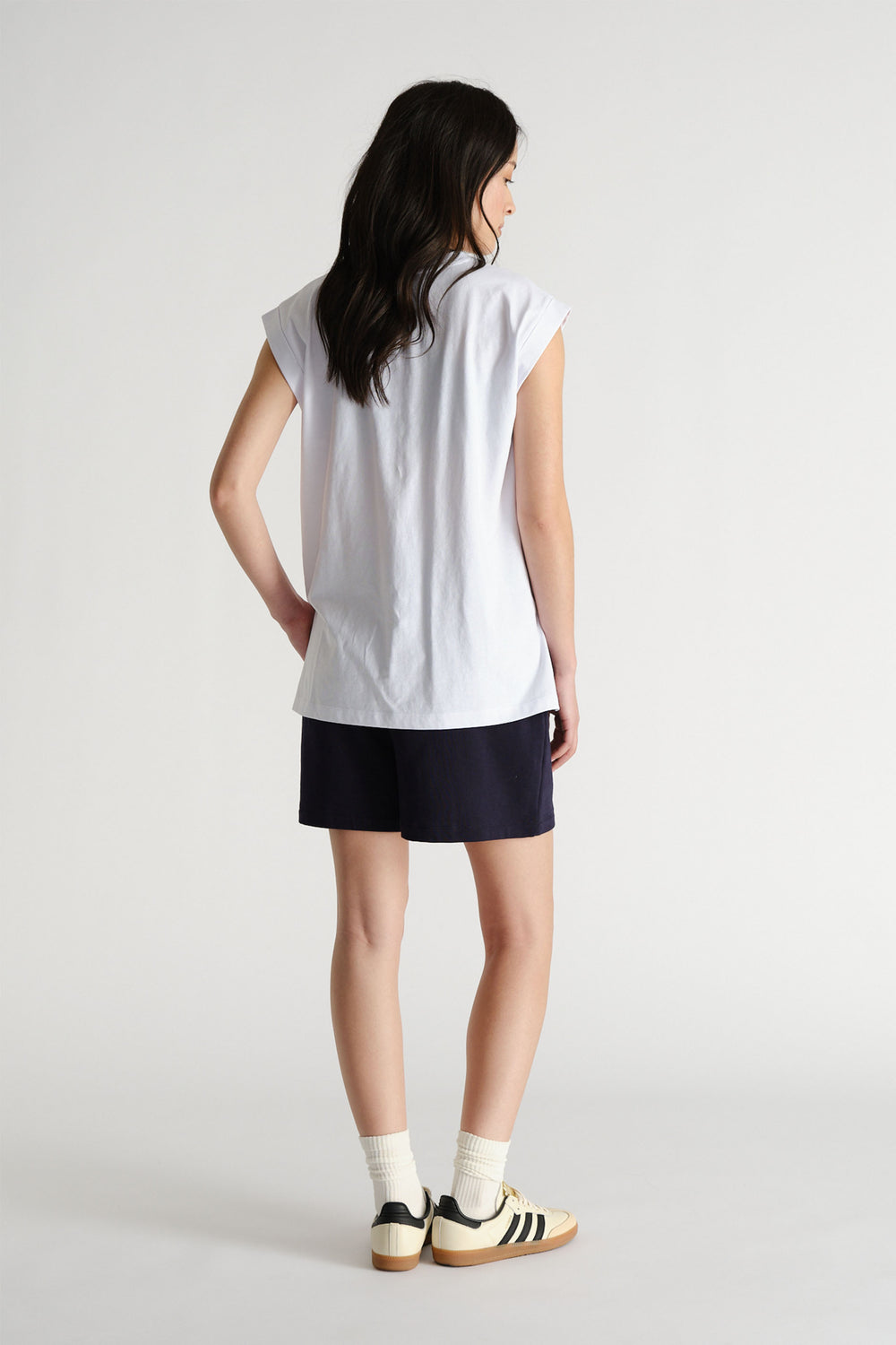Woman shown from behind wearing a relaxed white sleeveless tank with black shorts and retro sneakers for casual style