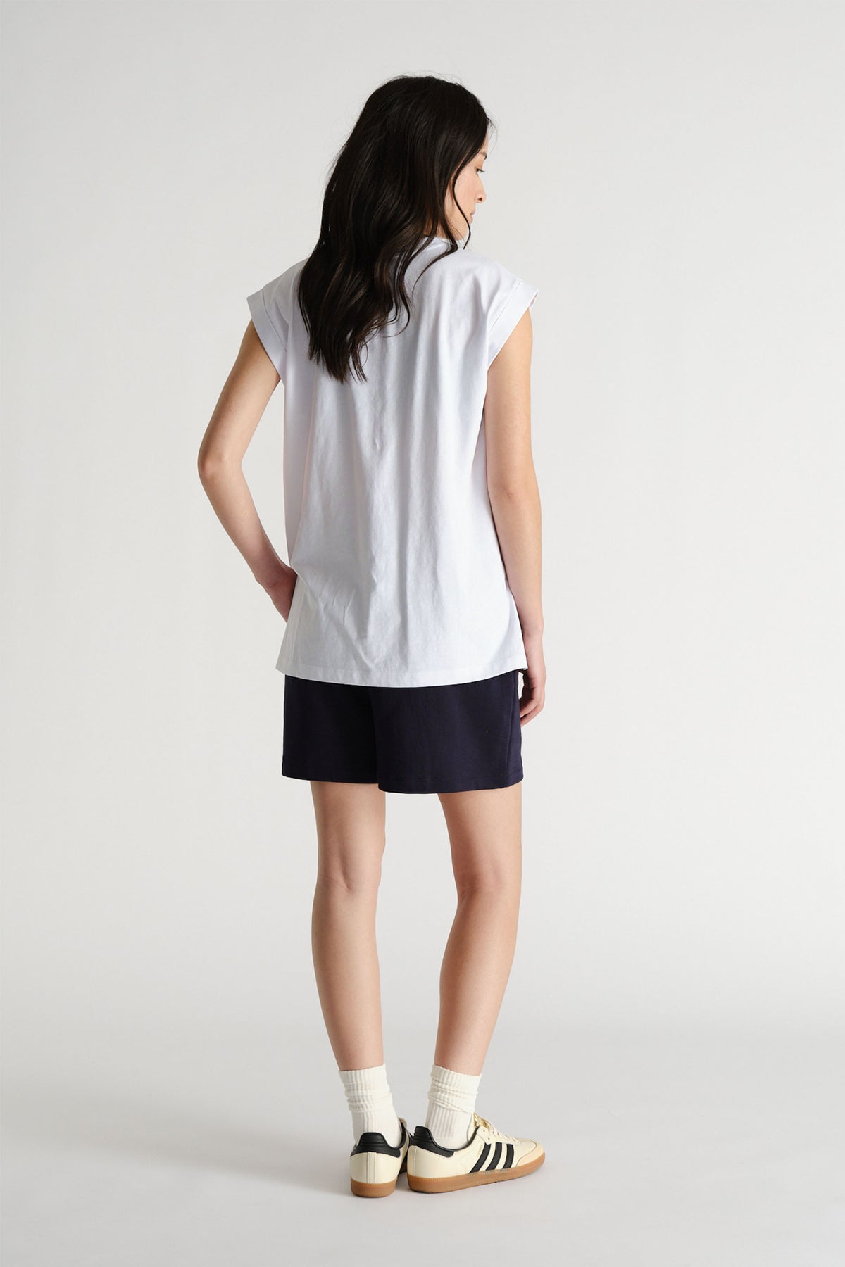 Woman shown from behind wearing a relaxed white sleeveless tank with black shorts and retro sneakers for casual style