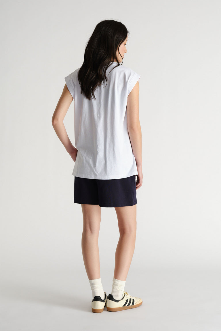 Woman shown from behind wearing a relaxed white sleeveless tank with black shorts and retro sneakers for casual style