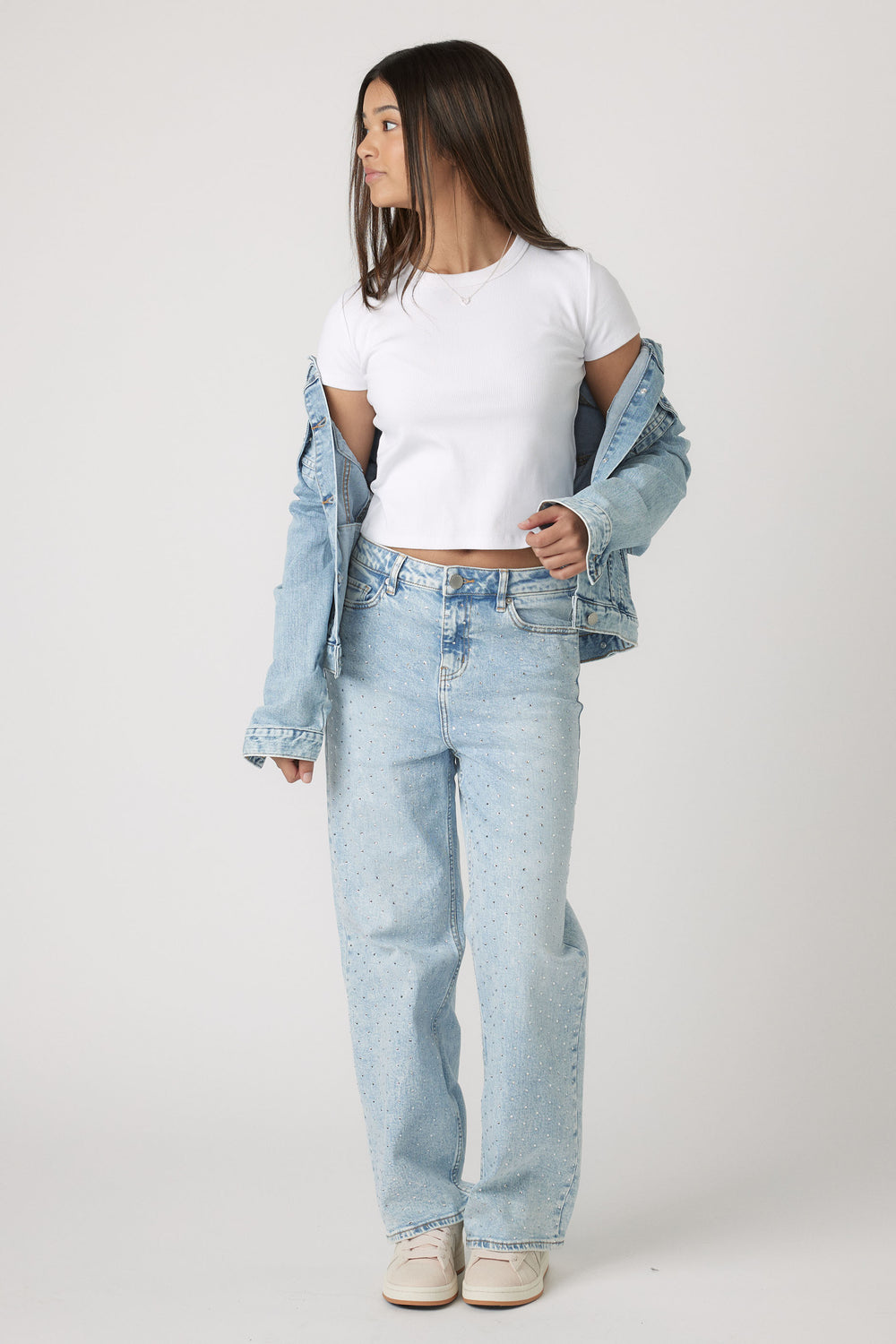 Teen girl styled in a white cropped tee layered with a light wash denim jacket and high-rise jeans for casual ease.